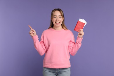 Happy young woman with passport and ticket pointing at something on purple background