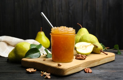 Photo of Delicious pear jam and fresh fruits on black wooden table