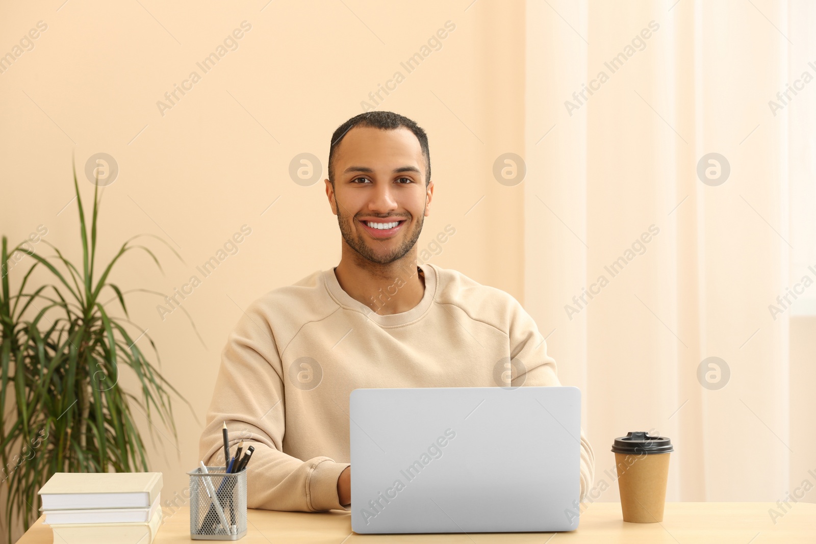 Photo of Portrait of smiling African American man with laptop at wooden table in room