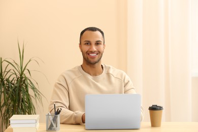Portrait of smiling African American man with laptop at wooden table in room