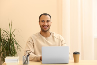 Photo of Portrait of smiling African American man with laptop at wooden table in room