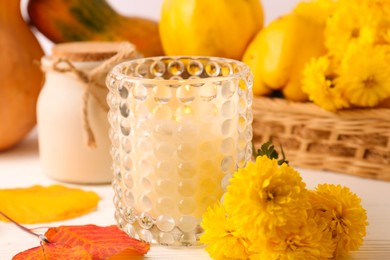 Photo of Burning candle, chrysanthemums and yellow leaves on white wooden table, closeup