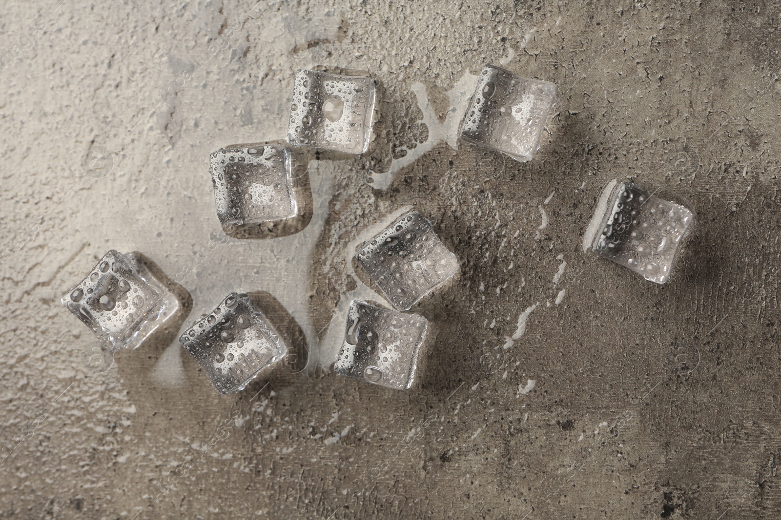 Photo of Melting ice cubes and water drops on grey textured table, flat lay