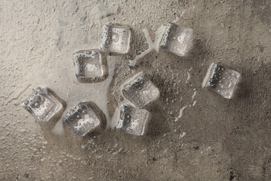 Photo of Melting ice cubes and water drops on grey textured table, flat lay