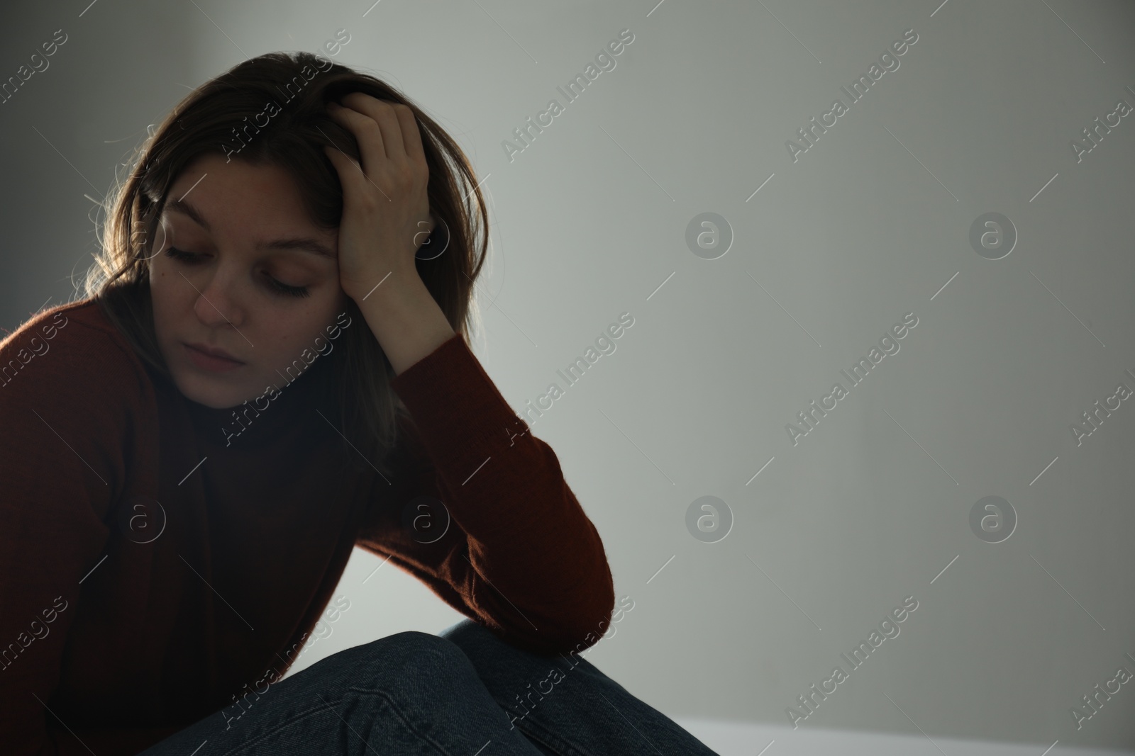 Photo of Sad young woman near grey wall indoors, space for text