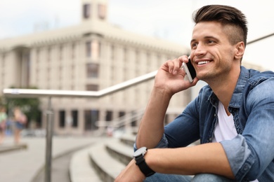 Portrait of handsome young man talking on phone outdoors. Space for text