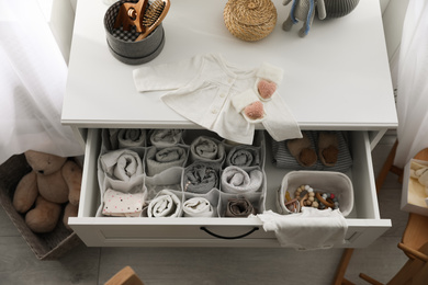Photo of Modern open chest of drawers with baby clothes and accessories in room, above view