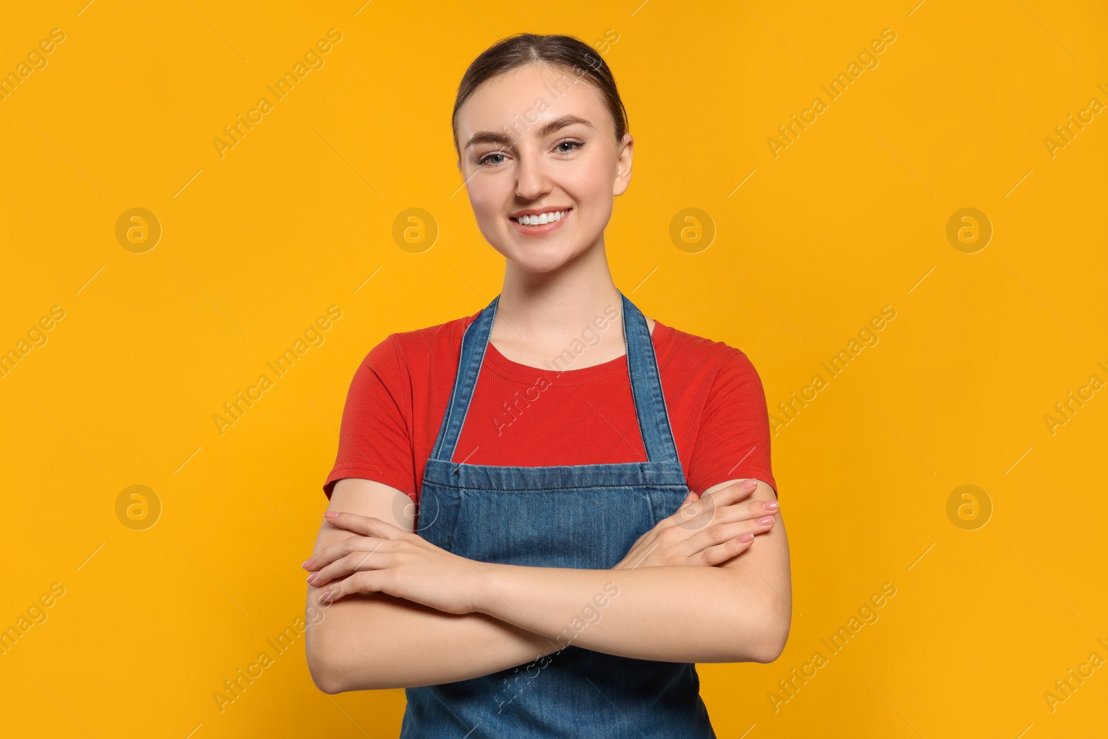 Photo of Beautiful young woman in clean denim apron on orange background