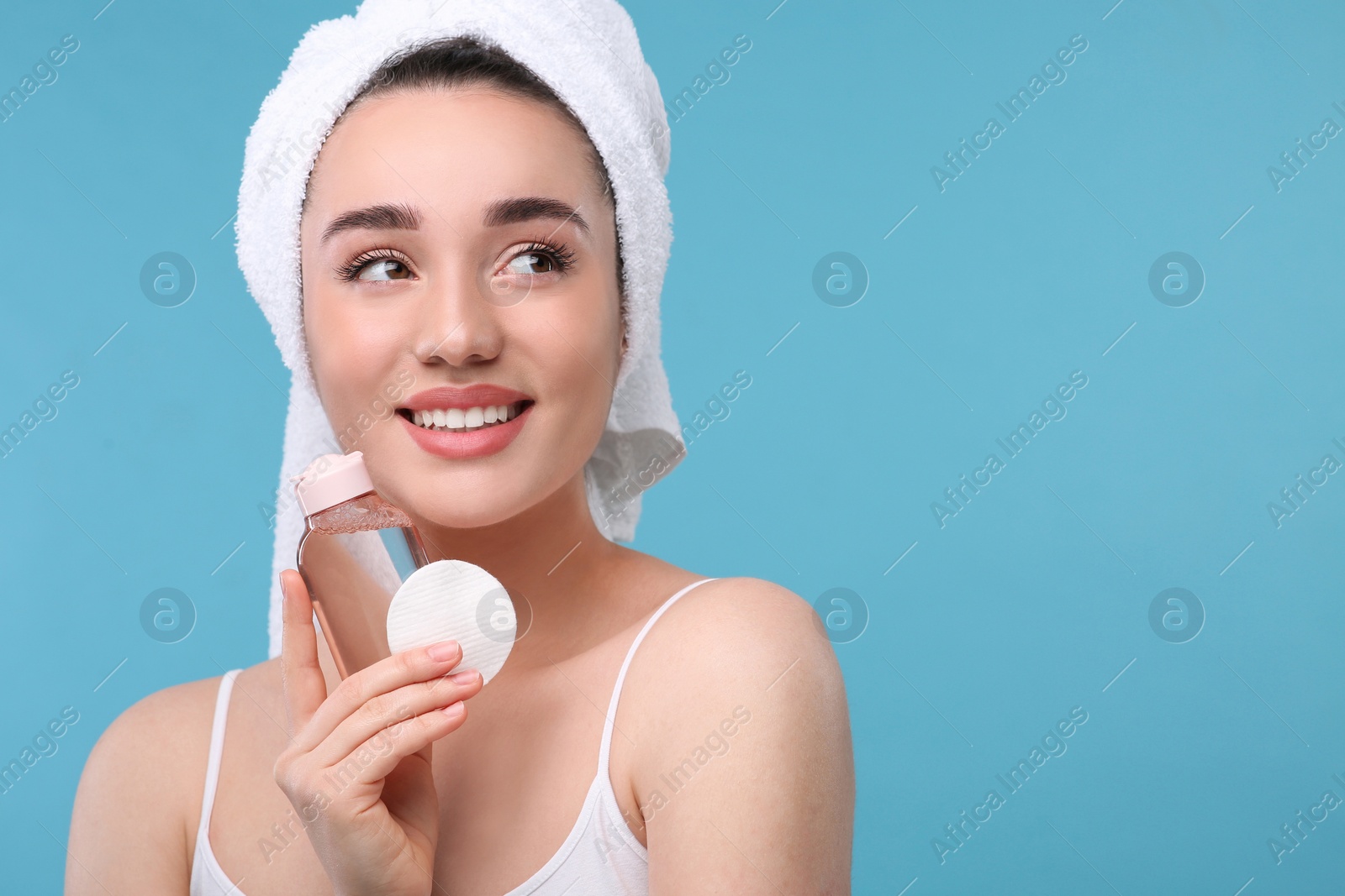 Photo of Beautiful woman with makeup remover and cotton pad on light blue background, space for text