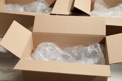 Photo of Many open cardboard boxes with bubble wrap on white wooden floor