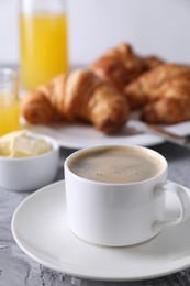 Tasty breakfast. Cup of coffee, butter and fresh croissants on grey table, closeup