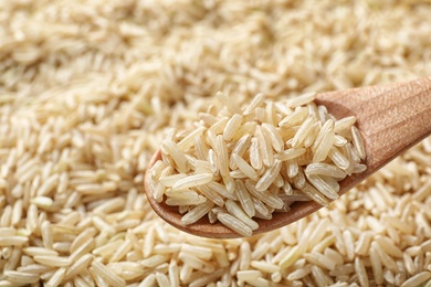 Photo of Wooden spoon with raw brown rice over cereal, closeup