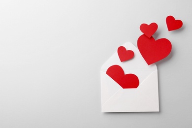 Red paper hearts and envelope on white background, top view