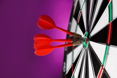 Photo of Red arrows hitting target on dart board against purple background