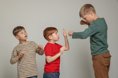 Boy with clenched fists bullying scared kids on light grey background