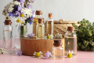 Photo of Aromatherapy. Different essential oils and flowers on pink wooden table