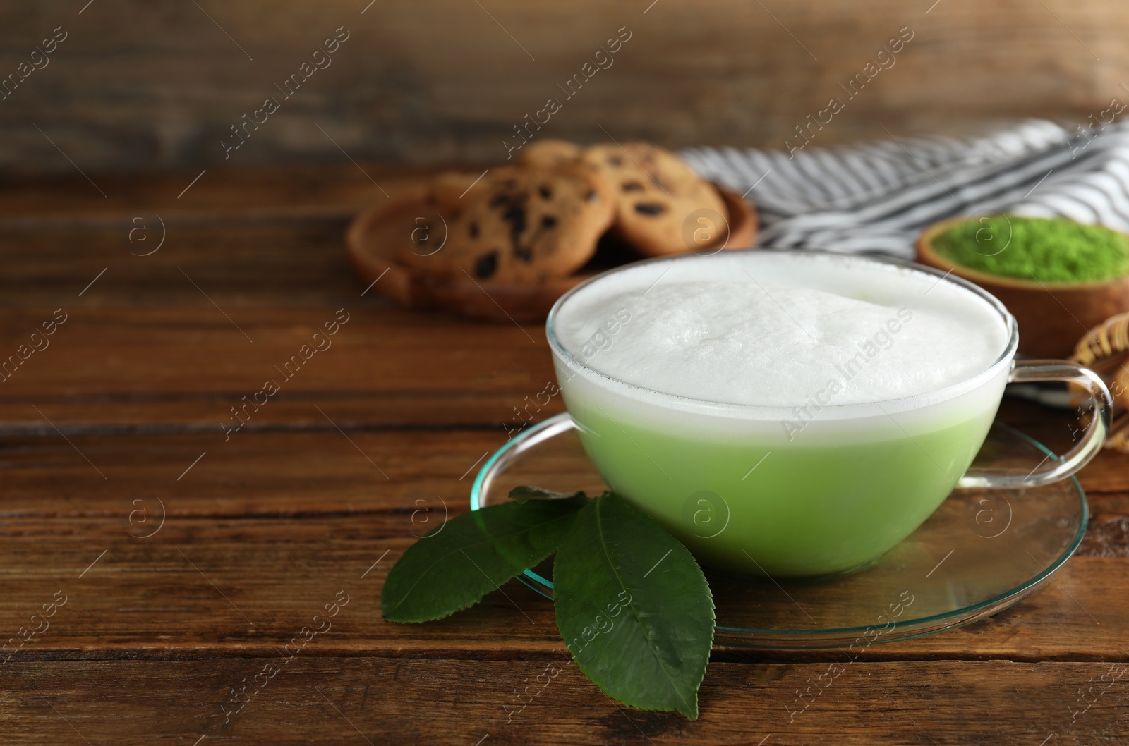 Photo of Cup of fresh matcha latte and green leaves on wooden table. Space for text