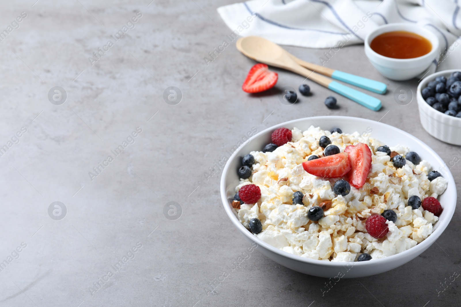 Photo of Delicious cottage cheese with fresh berries and honey served on light grey table, space for text. Tasty breakfast