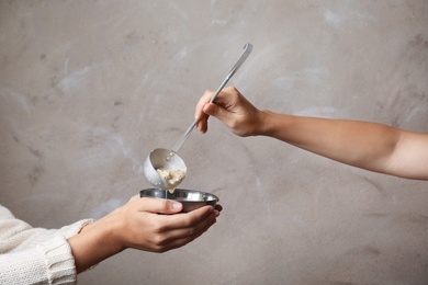 Volunteer putting food into bowl of poor woman on color background, closeup. Concept of help