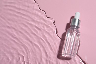 Bottle of cosmetic oil in water on pink background, top view. Space for text