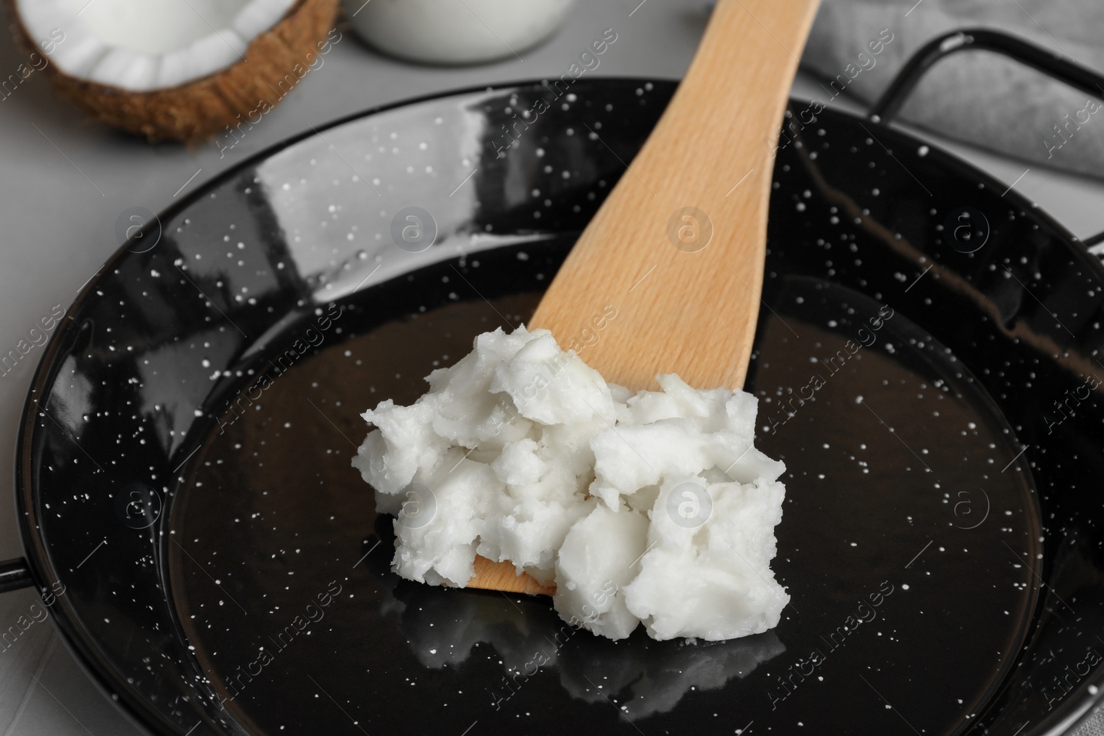 Photo of Frying pan with coconut oil and wooden spatula on light grey table, closeup