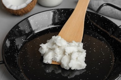 Photo of Frying pan with coconut oil and wooden spatula on light grey table, closeup