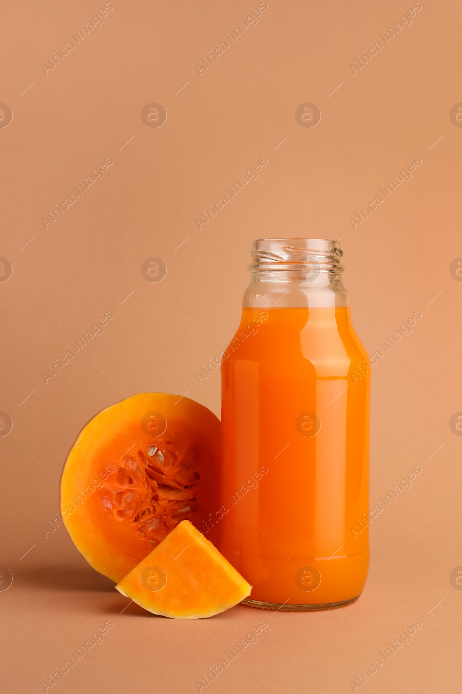 Photo of Tasty pumpkin juice in glass bottle and cut pumpkin on pale orange background