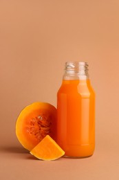 Photo of Tasty pumpkin juice in glass bottle and cut pumpkin on pale orange background
