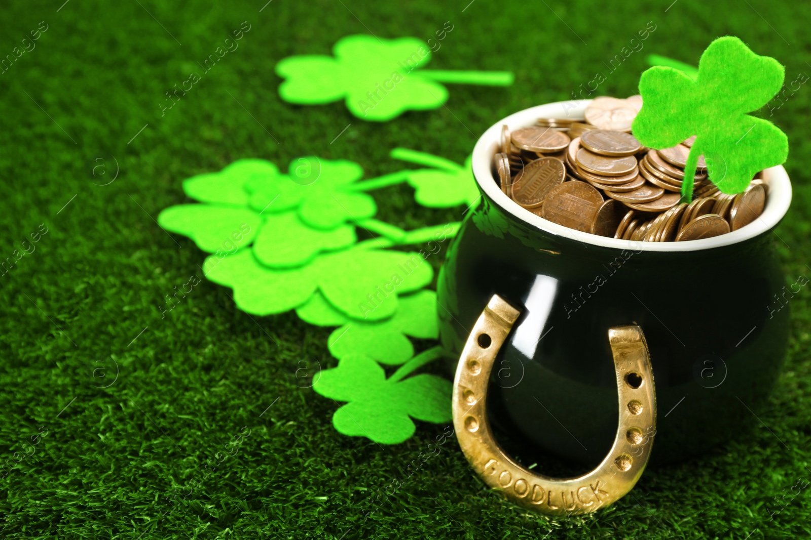 Photo of Pot of gold coins, horseshoe and clover leaves on green grass, space for text. St. Patrick's Day celebration