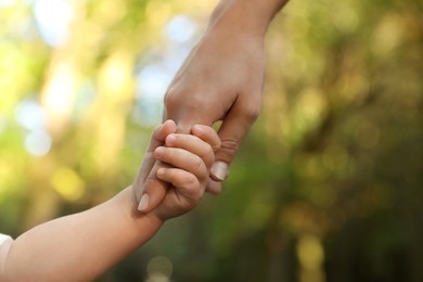 Photo of Daughter holding mother's hand outdoors, closeup. Happy family