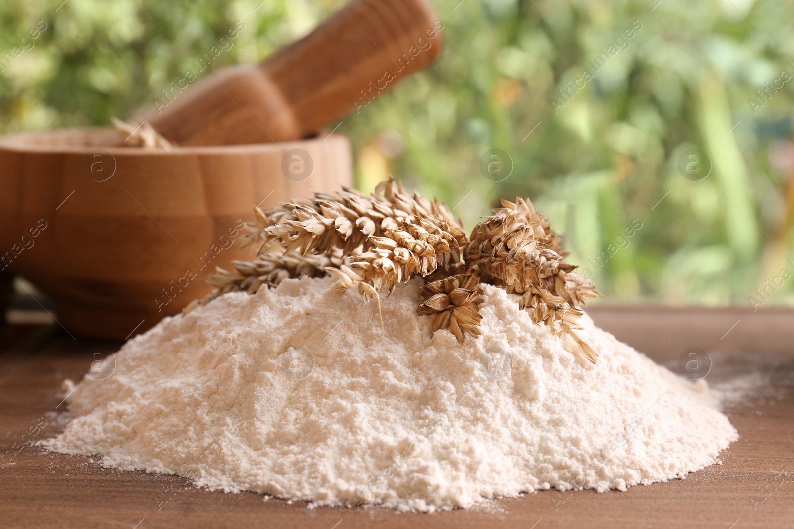 Photo of Pile of wheat flour and spikes on wooden board indoors, closeup