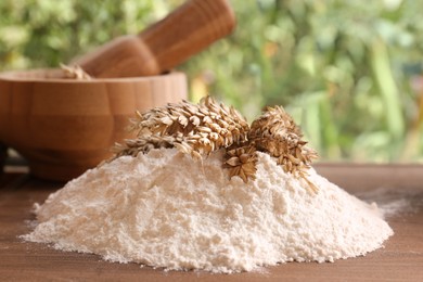 Photo of Pile of wheat flour and spikes on wooden board indoors, closeup