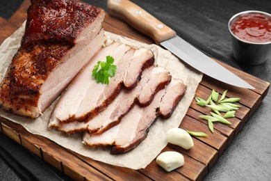 Photo of Pieces of baked pork belly served with sauce and parsley on black textured table