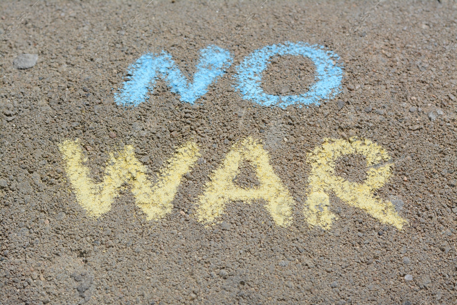 Photo of Words No War written with blue and yellow chalks on asphalt outdoors