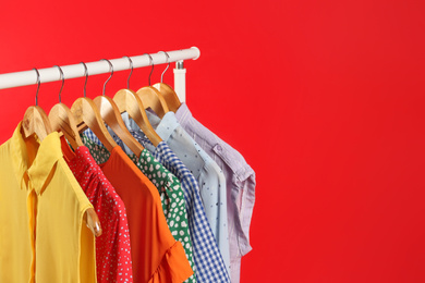 Bright clothes hanging on rack against red background, space for text. Rainbow colors