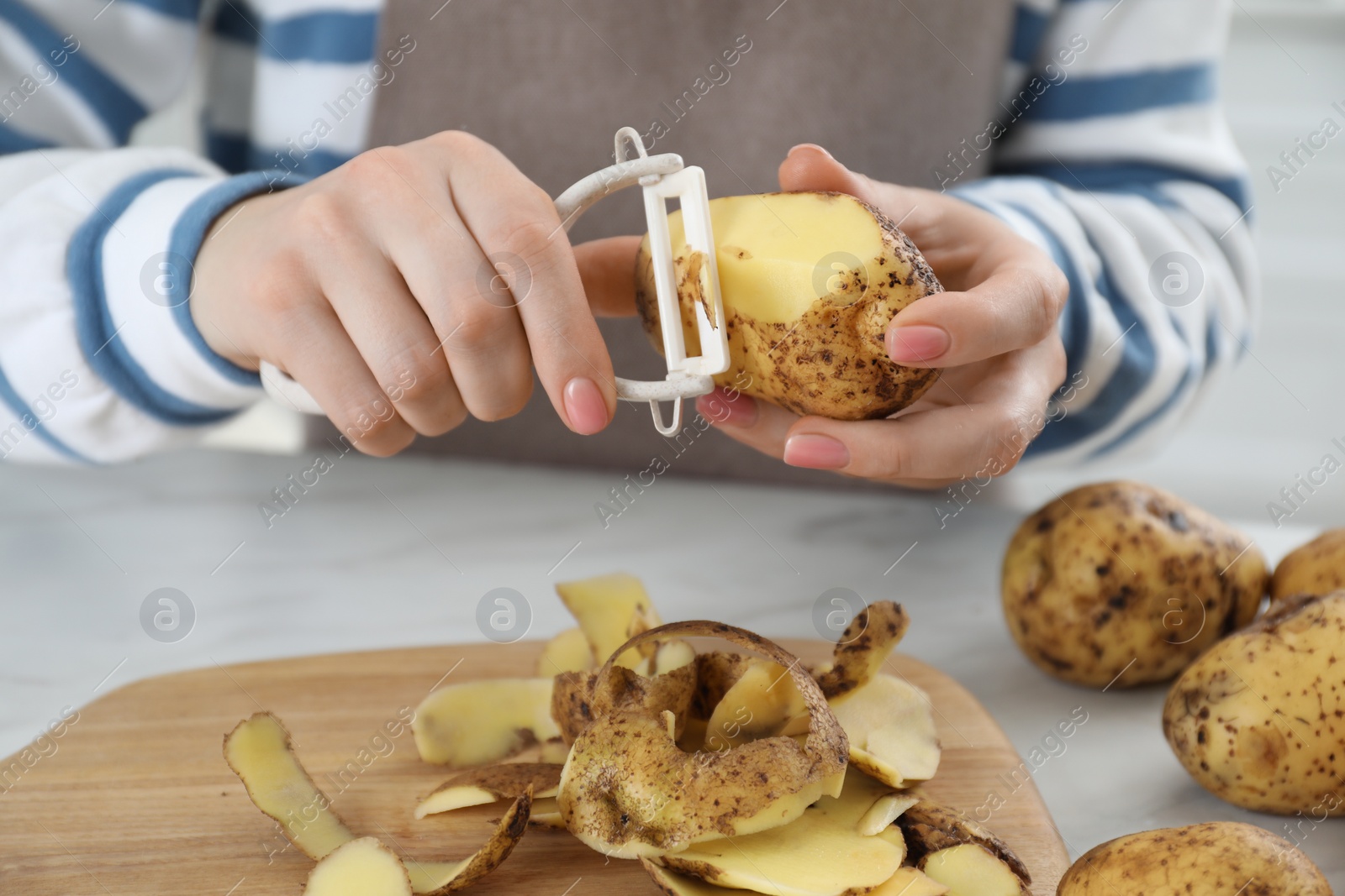 Photo of Woman peeling fresh potato at white marble table, closeup