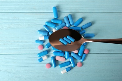 Spoon with weight loss pills on wooden background, top view