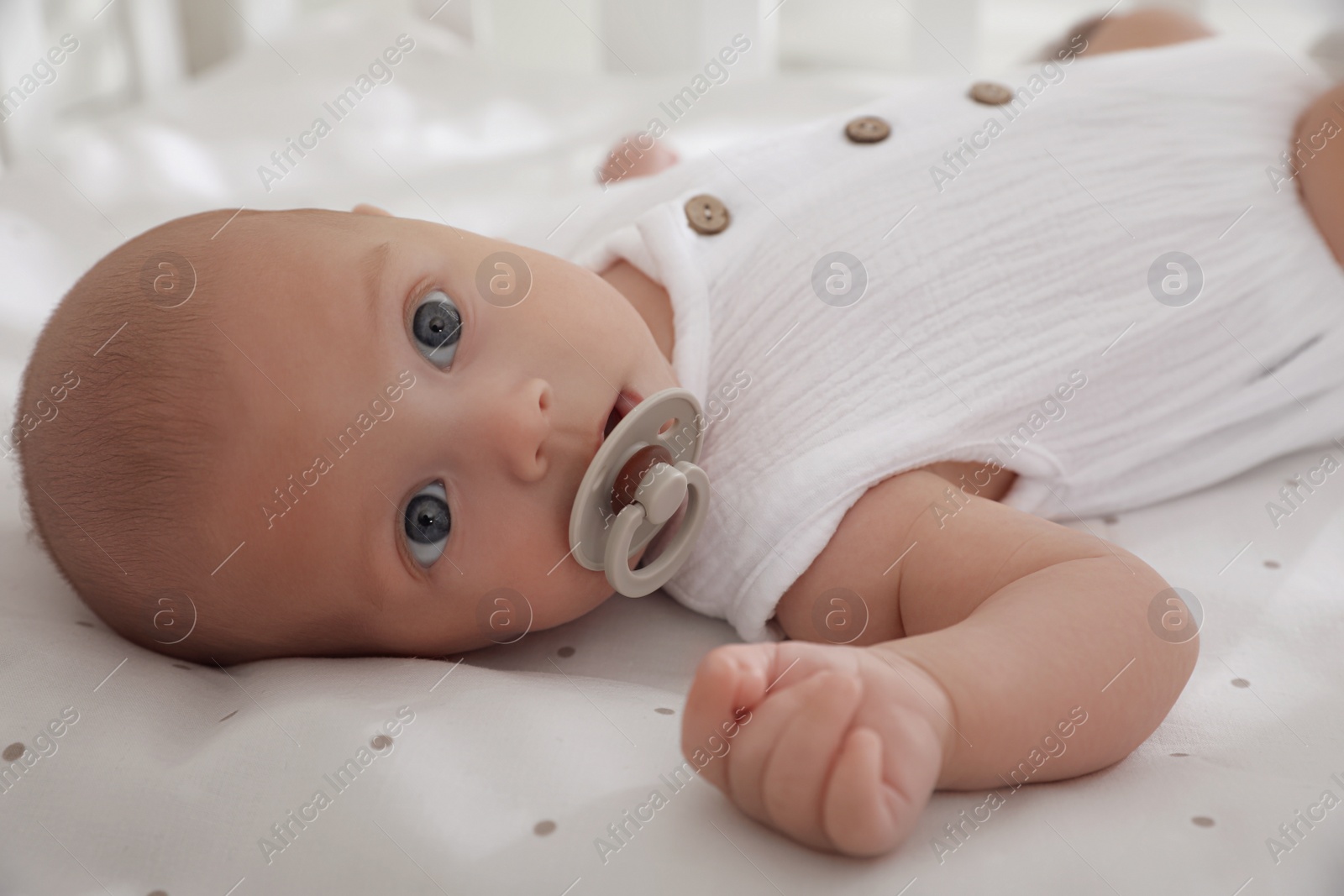 Photo of Cute little baby with pacifier lying on bed, closeup