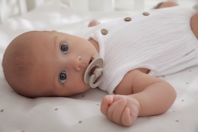 Photo of Cute little baby with pacifier lying on bed, closeup