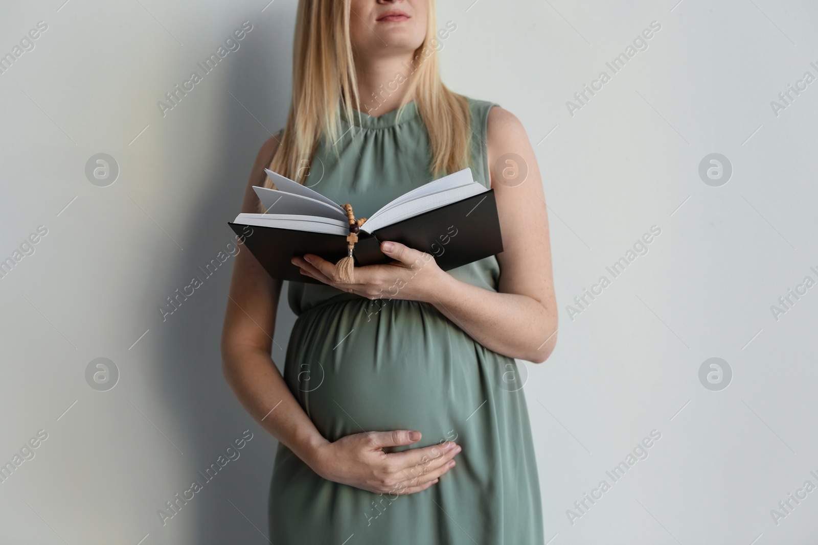 Photo of Young pregnant woman with Bible praying on light background