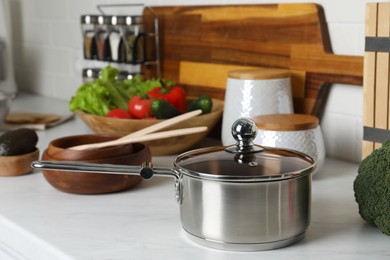 Photo of Metal saucepan, other cooking utensils and fresh vegetables on countertop in kitchen