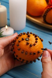 Photo of Woman decorating fresh tangerine with cloves at light blue wooden table, closeup