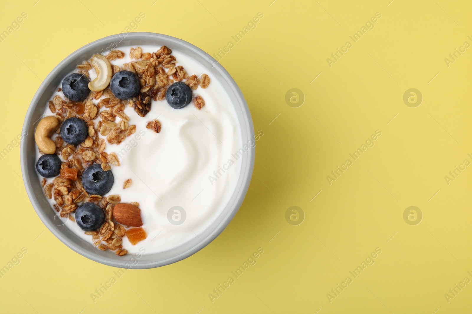 Photo of Bowl with yogurt, blueberries and granola on yellow background, top view. Space for text