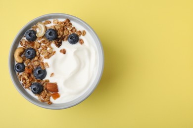 Bowl with yogurt, blueberries and granola on yellow background, top view. Space for text