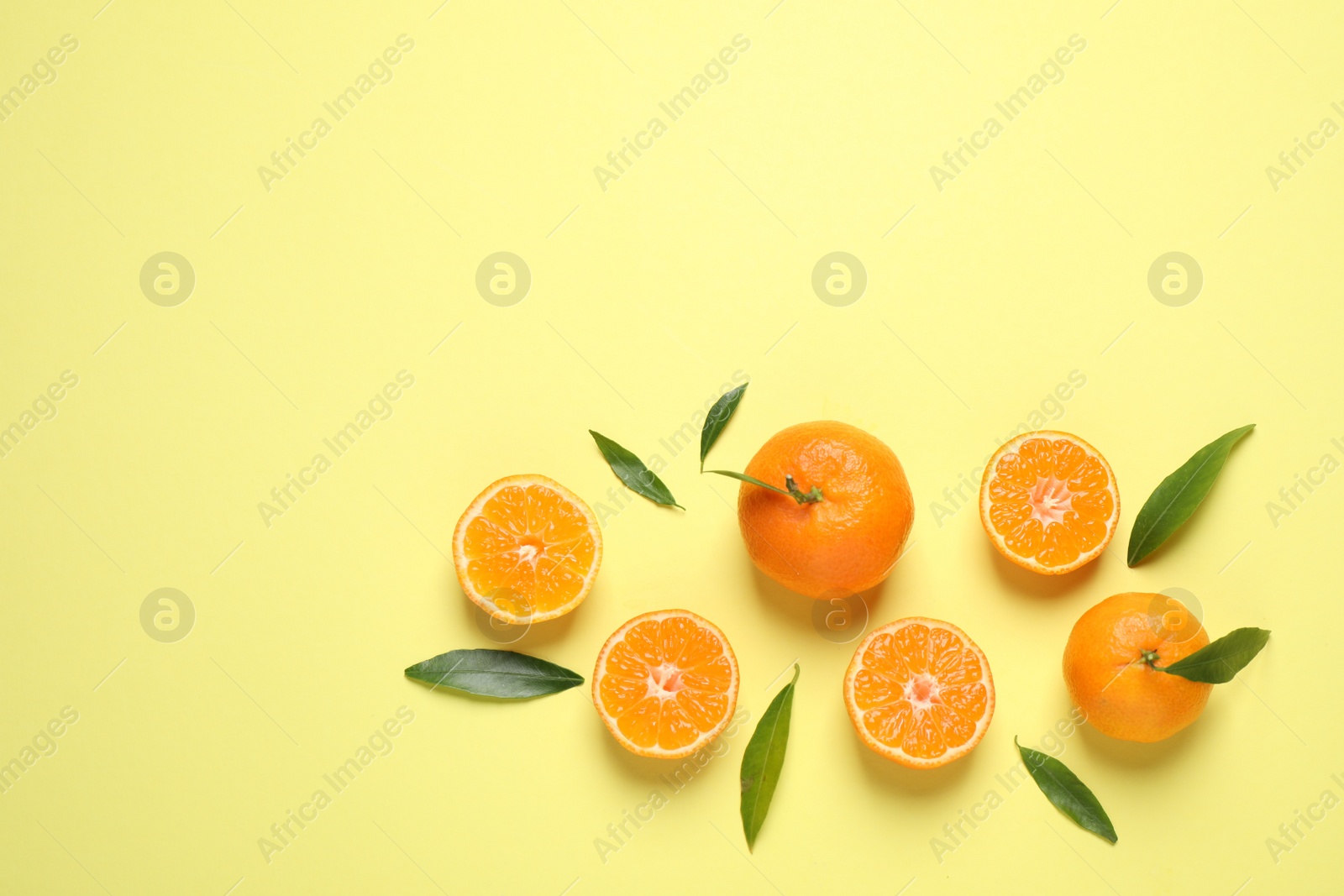 Photo of Flat lay composition with fresh ripe tangerines and leaves on light yellow background. Citrus fruit