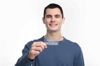 Young man with whitening strips on light background