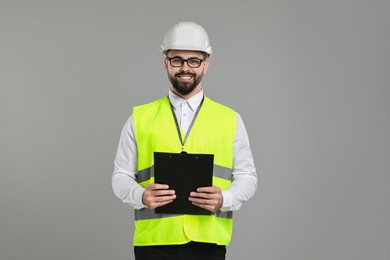 Photo of Engineer in hard hat holding clipboard on grey background