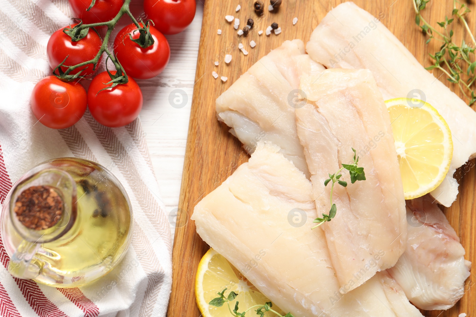 Photo of Pieces of raw cod fish, lemon, tomatoes and oil on white wooden table, top view