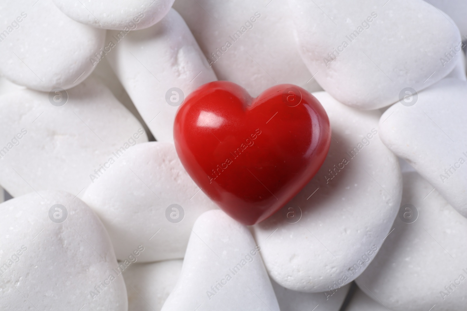 Photo of Decorative heart on white pebble stones, top view