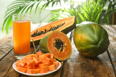 Photo of Fresh papayas and juice on wooden table against blurred background